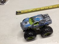 Rhino-themed monster truck toy with blue flames and oversized wheels shown next to a tape measure for scale.
