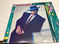 Front cover of the Jump Up album by Elton John, showing artist in teal suit and hat.