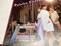 Front cover of the 'Energy' album by the Pointer Sisters showing three women posing in an industrial setting at night.