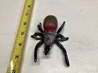 Photo showing the Sectaurs Toxic action figure next to a tape measure for size reference, displaying the insect-like shape and red-black coloring.