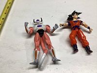 Photo showing two Dragonball Z figures of Goku and Frieza laid on a white surface with ruler for scale.