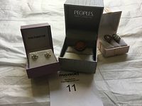 Three jewelry boxes each containing a piece: Michael Hill silver-tone earrings, Peoples brooch with reddish stone, and green gemstone drop earrings.