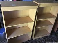 Two light wood finish bookcases side by side showing their front, each with three shelves and minor visible damage on the bottom panels.