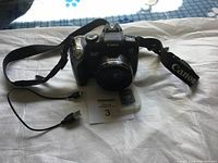 Canon PowerShot SX20 digital camera with strap, microSD adapter, USB cable, and MaxSold paper on white sheet background