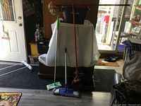 Photo showing a spin mop bucket in red and black with a wringer, a blue flat mop, a red broom with a dustpan, and a green and white mop.