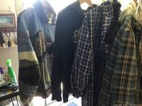 Photo showing five men's coats on hangers, including camouflage, solid black with logo, and various plaid patterns.