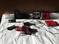 Three vintage Zippo lighters in unique cases, Kodiac digital camera, wallet, and leather accessory displayed on white sheet against wooden background