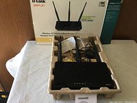 View of D-Link AC750 Wireless Router with three high-gain antennas, Ethernet cable and power adapter inside molded packaging with original box behind it.