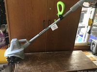 Full side view of the Earthwise electric rototiller resting on a wooden surface with a green handle grip visible