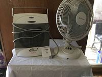 Photo showing Sunbeam heater and Westpoint table fan side by side on a table with power cords visible.