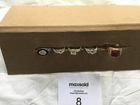 Photo showing five distinct rings arranged in a row on a brown box, with a MaxSold auction number 8 paper below.