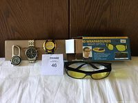 Photo of night vision glasses in box with three watches on white cloth background