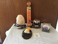 Photo of salt lamp, eagle plaque, turkey decoy in box, Taz figurine, and lighted eyeball candle holder on table.
