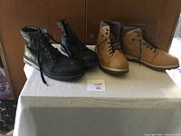 Photo shows two pairs of men's hiking boots, one black and one tan, both size 13, placed on a white surface against a wooden background.