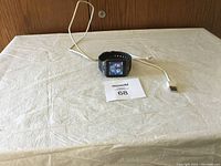 Front view of the smartwatch powered on displaying the time, date, and charging cable connected.