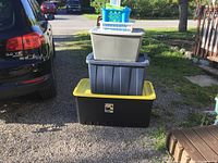 Photo of three plastic storage totes stacked outdoors on gravel next to a vehicle and deck.