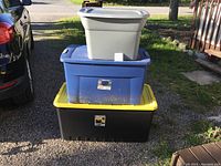 Stack of three plastic storage totes outdoors on gravel and grass