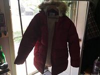 Photo of a red women's extra large heavy winter coat by Mountain Ridge hanging on a hanger, front view showing the zipper open and faux fur hood trim.