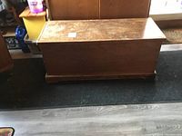 Full view of the rectangular solid wood trunk with hinged lid, showing surface wear and scratches