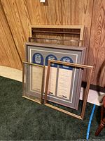 Full view of the framed Amtrak menus and empty frames leaning against wood panel wall on green carpet.