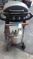 Front view of Nexgrill barbecue mounted on custom steel cart showing propane tank and control knobs.
