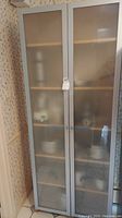 Full frontal view of tall pantry cabinet with frosted glass doors, white frame, and light wood interior.