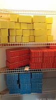Shelves with stackable cardboard bricks in yellow on the top shelf, red on the middle shelf, and blue on the bottom shelf.