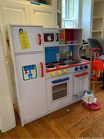 Front view of the full children's play kitchen set with refrigerator, stove, sink, microwave, and cleaning accessories.