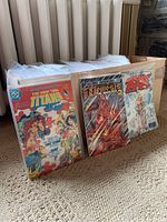 Box of comic books in plastic sleeves showing front covers of Teen Titans, Nemesis The Warlock, and another comic.