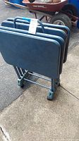 Set of four blue folding tables stacked on a blue metal folding stand. Tables measure approximately 23x15 inches.