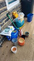 Outdoor wooden deck with corn plant in orange pot, bags of soil and perlite, multiple plant pots, watering can and blue plastic container.
