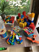 Full spread of lot contents including Mega Bloks pieces, wooden shape sorter, soft fabric toy cube, airplane, and puzzle pieces.