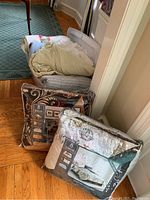 Photo of folded and packaged linens including comforters, blankets, quilts, and duvet covers in a basket on the floor.