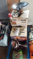 Image of Heat Demon propane stove placed on top of its original Hillary box, along with portable lamp and mosquito coil box in foreground