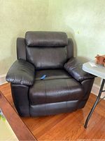Front and angled views of the dark brown leather-like recliner chair showing the attached cushions, armrests, and minor wear on the material.