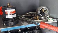 Various plumbing components and accessories including hoses, connectors, and fittings arranged on shelf with pump in background.