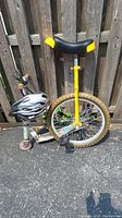 Side view showing unicycle with yellow seat, thick tire, pedal, and adjacent scooter with white helmet hanging on handlebar.