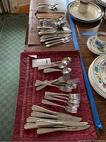 Overview of wooden chopsticks and multiple pieces of Oneida stainless steel silverware including forks, knives, and spoons on dining table.