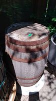 Weathered wood barrel with rusty metal bands in outdoor setting, photographed from above and slightly to the side showing full barrel and top surface.