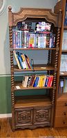 Front view showing full height of bookcase with four shelves and bottom cabinet; shelves hold books and VHS tapes.