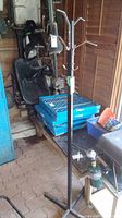 Full view of metal coat rack standing upright in a shed, showing hooks and upper part of the rack.