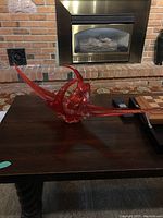 Red abstract glass sculpture on a dark wooden table in front of a brick fireplace.