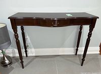 Front view of the wood hall table showing turned legs and single drawer with metal handle