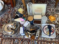 Top-down view of assorted kitchenware items including glass casserole dish, fish mold, storage jars, pepper grinder, utensils, and plates on patterned carpet.