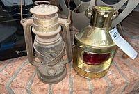 Two metal lanterns placed side by side on brick surface, showing a rusted oil lantern and a polished brass lantern.
