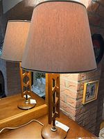 Front and side view of a Mid-Century Modern style table lamp with wooden base featuring geometric cutouts and beige fabric lampshade, showing general appearance and condition.