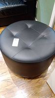Close-up photo showing the top surface with tufted button design and black faux leather upholstery.