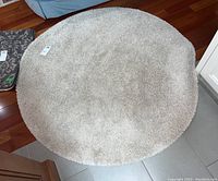 Top view photo of round cream Ikea area rug placed on tiled floor, showing shaggy texture and round shape.