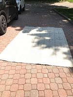 Full view of light-colored rectangular rug with anchor motifs, spread on outdoor pavement.