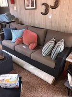 Full view of the sofa showing the three-seater design with brown cushions and various colored decorative pillows (not included).